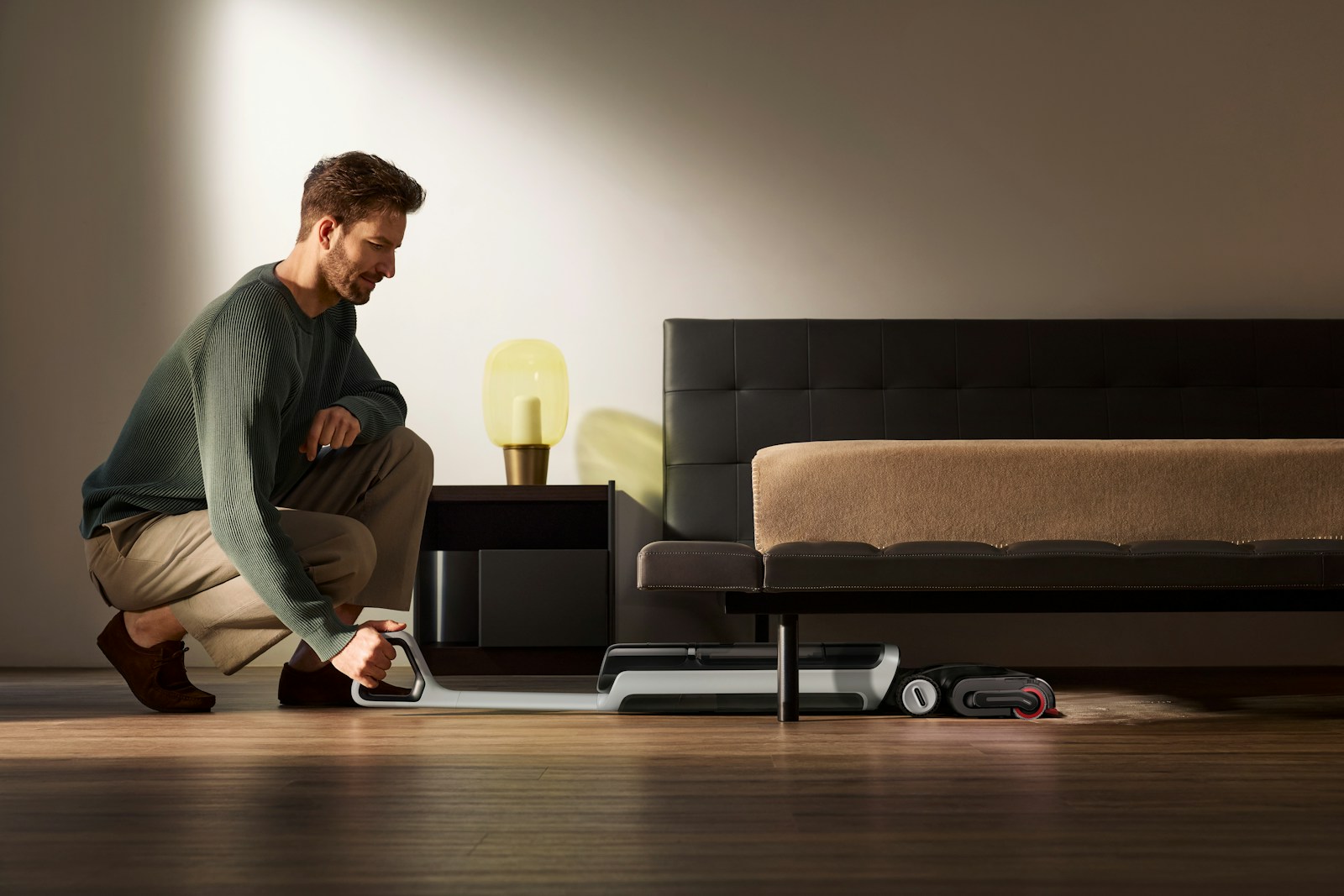 Man vacuuming under a bed with a robot vacuum